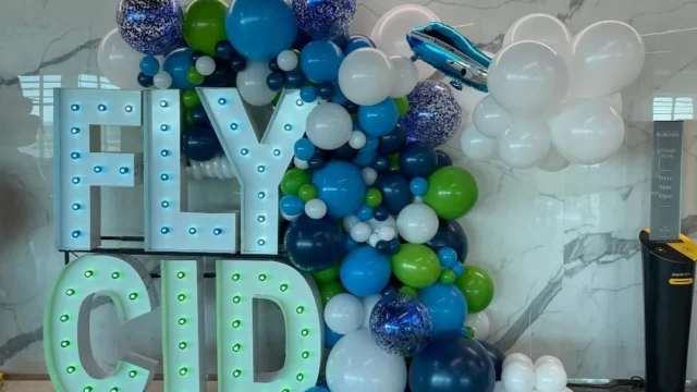 light up marquee spelling FLY CID with multi colored balloon garland