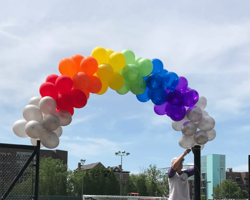 a guy putting up a small colorful balloon arch outside