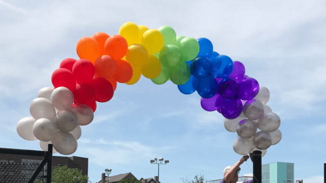 a guy putting up a small colorful balloon arch outside